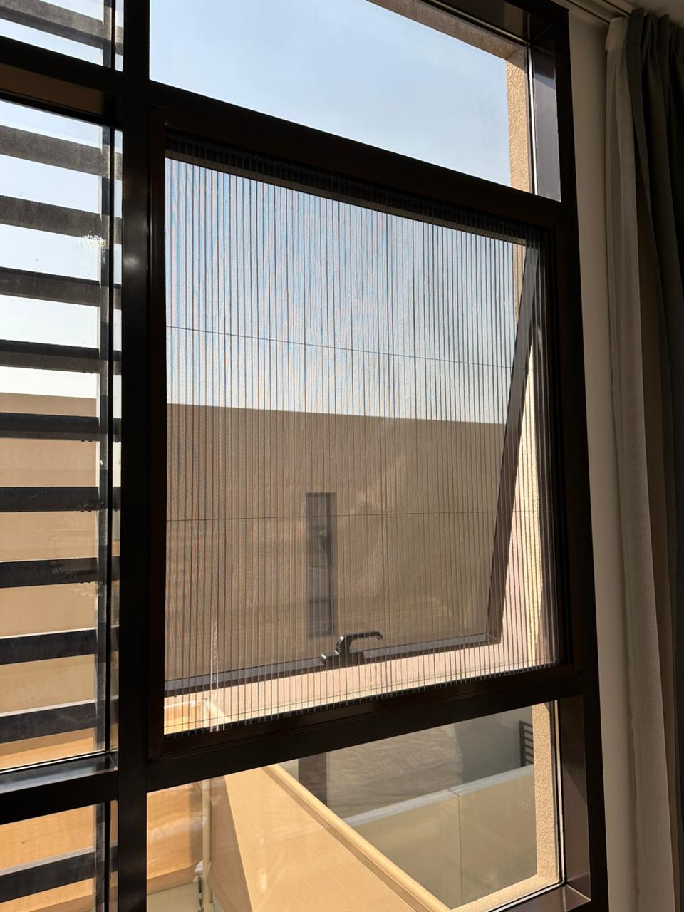 Custom fly screen on The Meadows villa bedroom window overlooking mature garden and lake, dark grey mesh white frame, Dubai