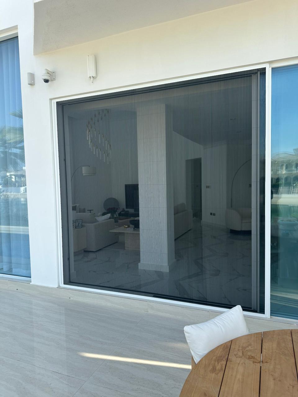 Retractable pleated fly screen on Downtown Dubai apartment balcony door, white aluminium frame black mesh, Burj Khalifa view preserved